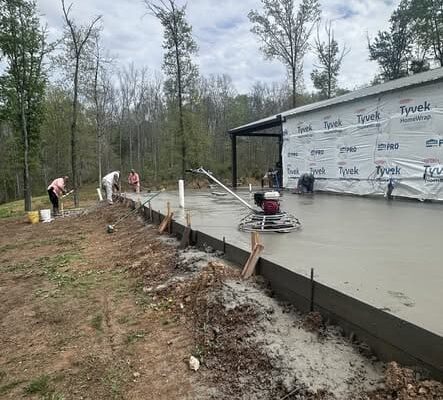 Workers smooth and finish a newly poured concrete slab in Lyles, TN as part of a 1,100-square-foot home addition project